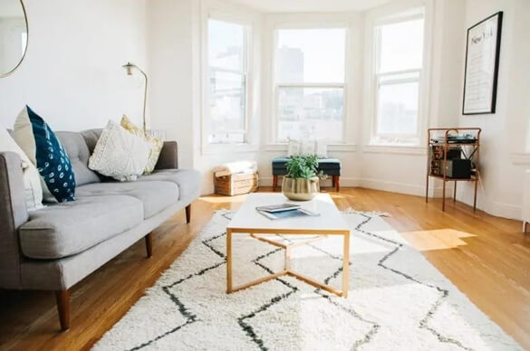 phòng khách có cửa sổ đơn giản phong cách châu Âu hiện đại. Sàn gỗ với thảm ziczac màu trắng, sofa xám.